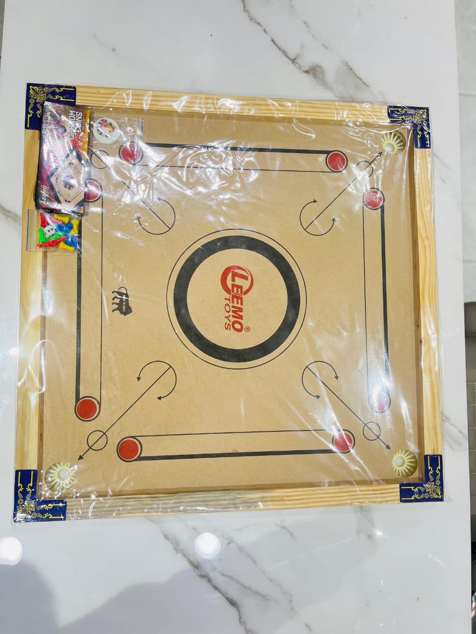 samstoy in wooden carrom board with ludo game in plastic wrap showing beige board red and black markings and pieces