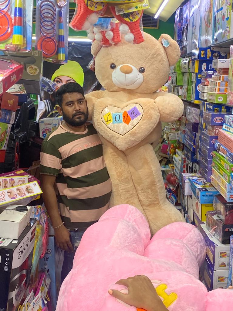 Man in toy shop holding large plush bear with heart reading LOVE big teddy bear In Ahmedabad Gujarat online India