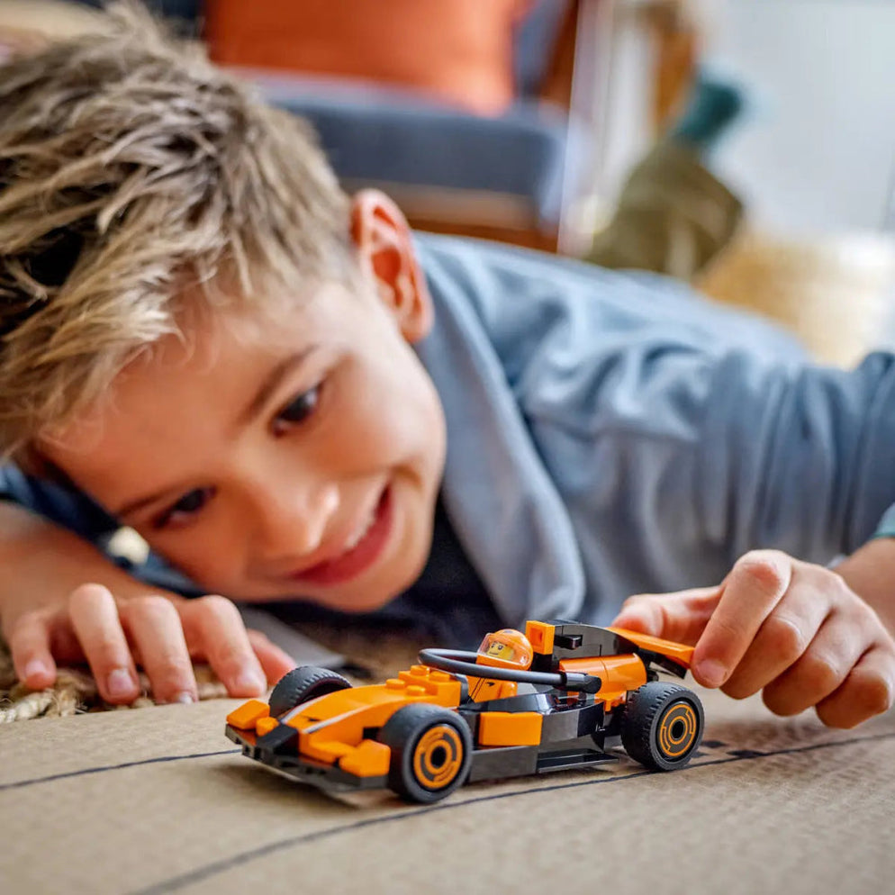 Smiling boy playing with an orange LEGO City Formula 1 Race Car best price Ahmedabad Gujarat India . toy car on floor