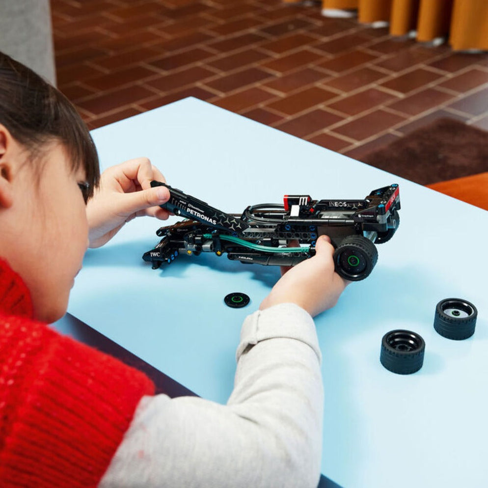 Child assembling Lego Technic Mercedes F1 car India set on blue table with spare tires and black chassis